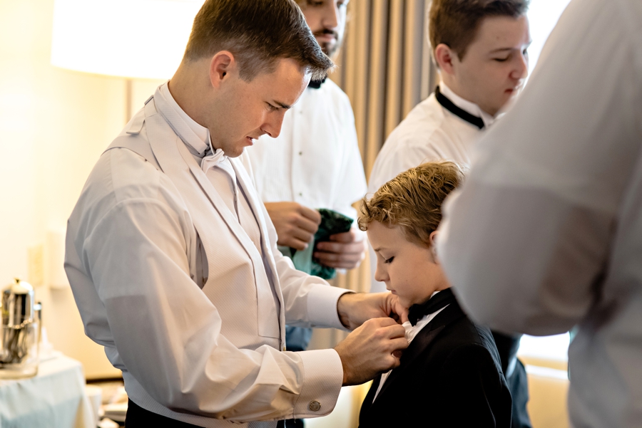 A groom helps the ring bearer with his tie.